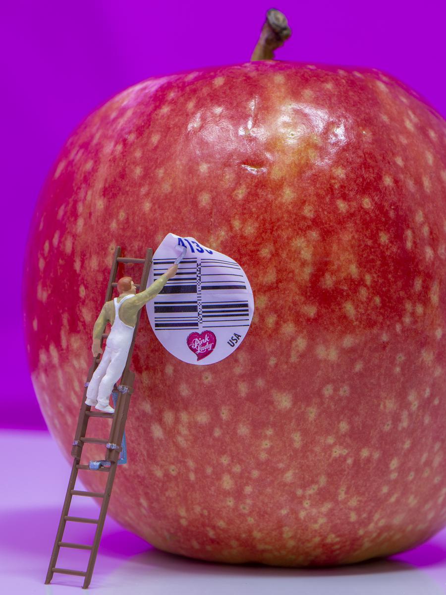 Human figurine on a label propped against an apple, putting on the barcode sticker