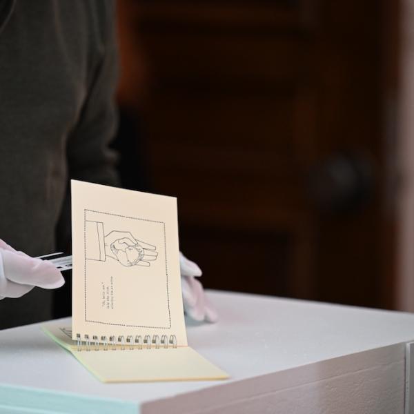 Individual uses tweezers to gently look through a booklet of drawings